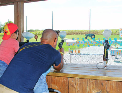 Father and son aiming paintball guns at colorful targets in a farm setting, showcasing a family-friendly attraction at Cherry Crest Adventure Farm.