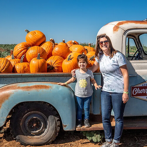 Family enjoying a day at Cherry Crest Adventure Farm, posing beside a vintage truck filled with freshly picked pumpkins in a sunny pumpkin patch.