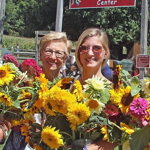 u-pick sunflowers Women holding vibrant bouquets of sunflowers and zinnias at Cherry Crest Adventure Farm's U-pick flower field, showcasing a joyful experience in a sunny outdoor setting.